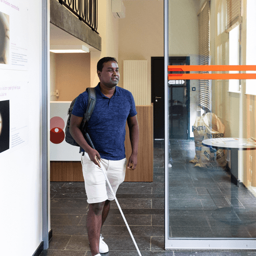 Un homme se déplace avec une canne blanche dans le couloir d'un bâtiment.