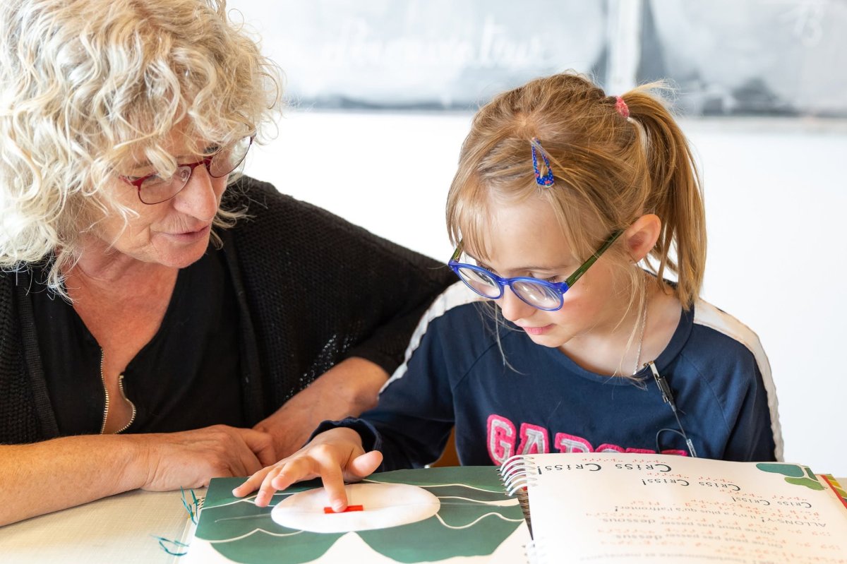 Une femme accompagne une jeune fille portant des lunettes bleues dans une activité de découverte tactile.
