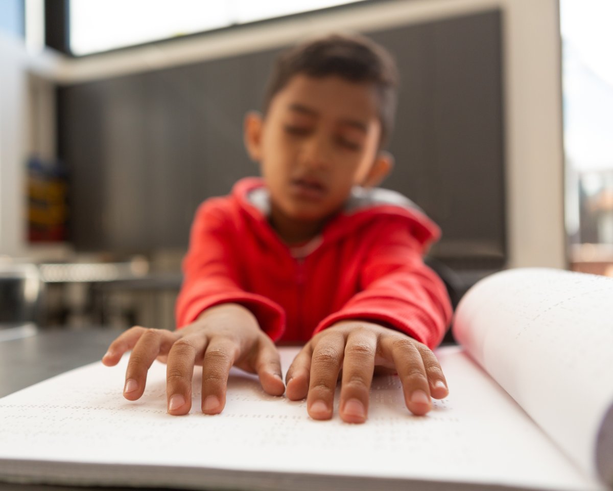 Un jeune garçon explore du bout des doigts les pages d'un livre en braille ouvert devant lui.